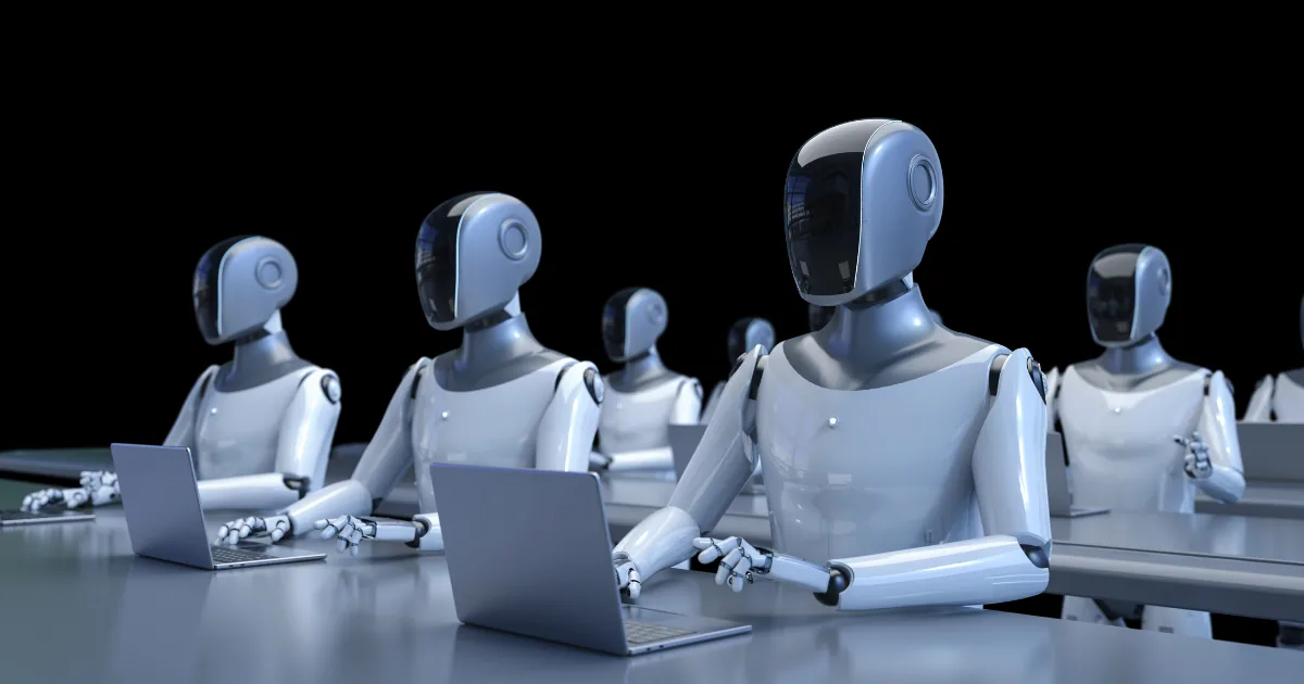 A row of white humanoid robots sitting at desks typing on laptops